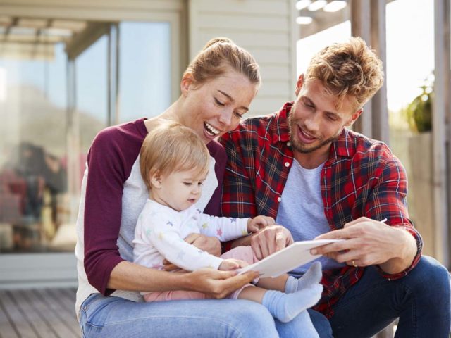 Young family sitting and smiling at camera outside